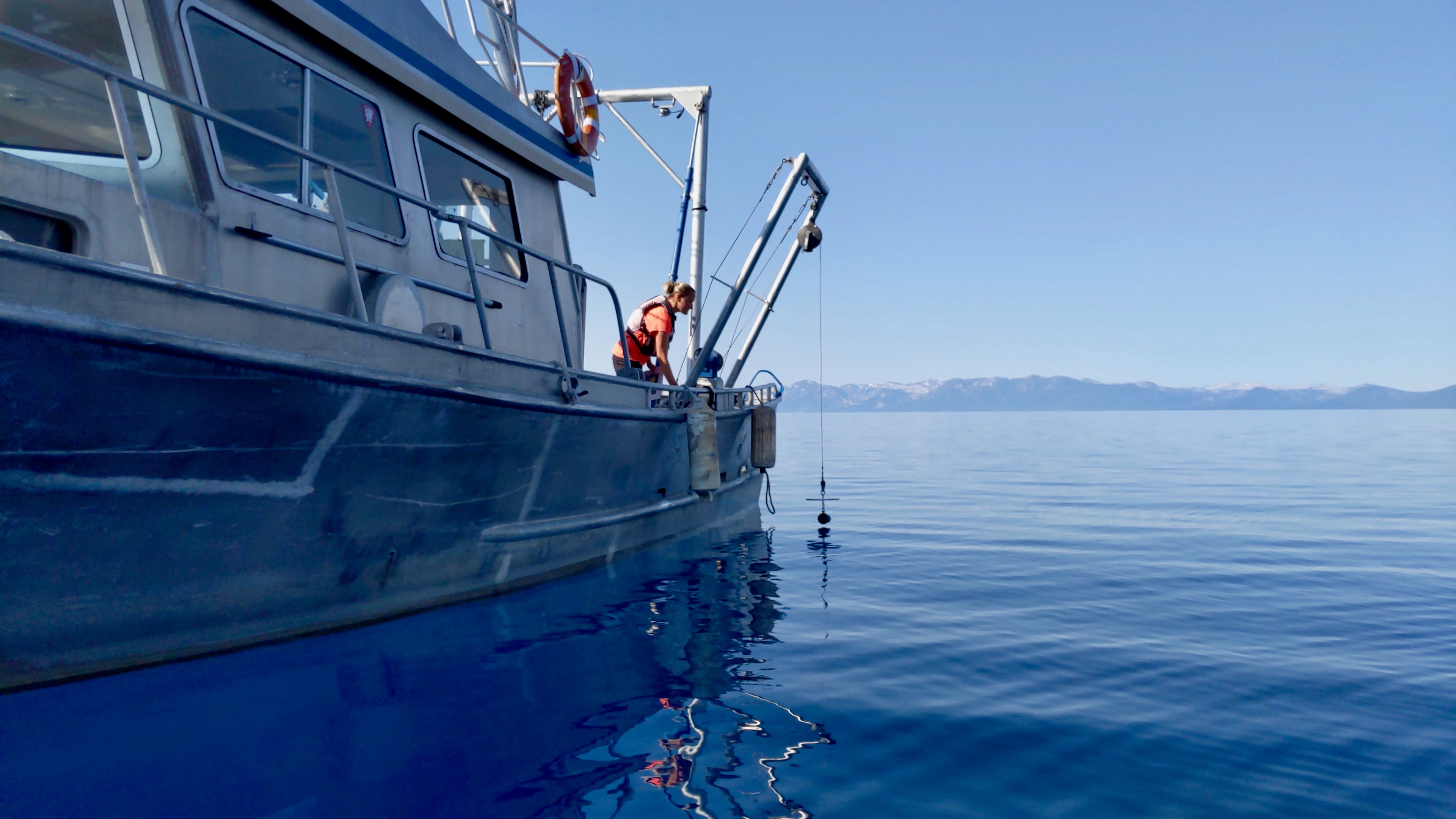 Female scientist lowers a Secchi disk from a research boat into Lake Tahoe to measure lake clarity.