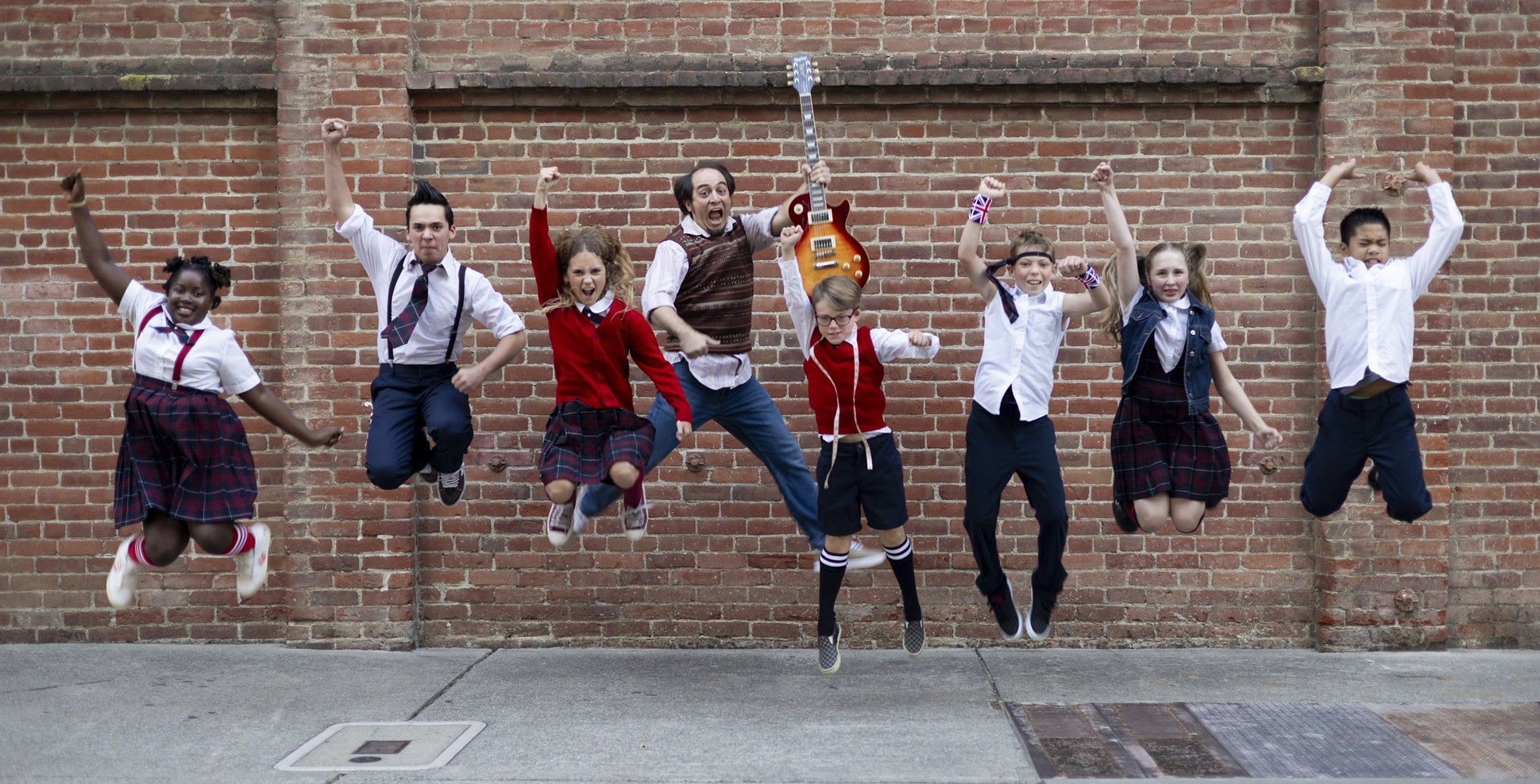 Student actors in costume jumping into air in front of a brick wall