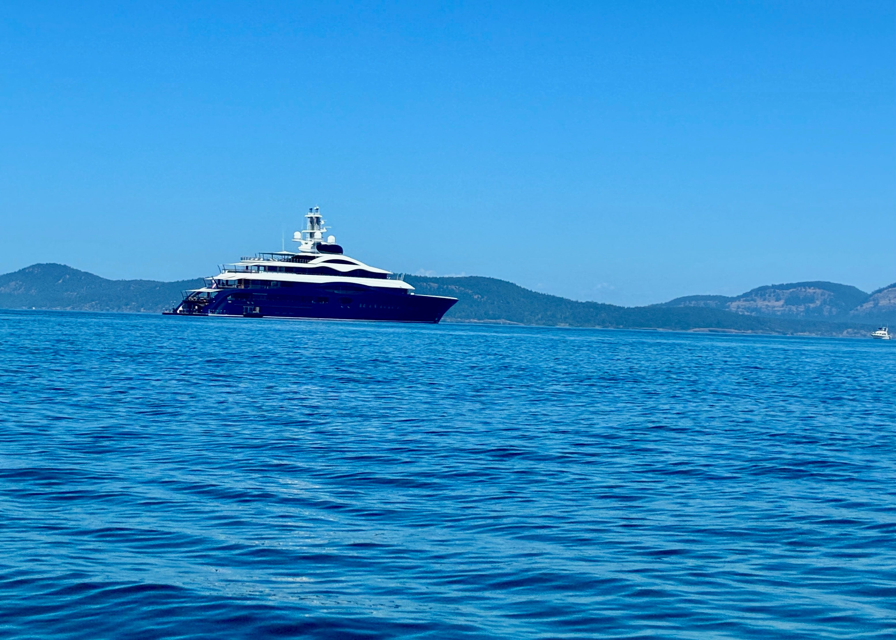 Luxury yacht on calm blue sea with distant island hills under clear sky