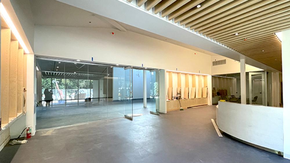 The unfinished lobby currently features gray tiled flooring, vertical windows that take up half of the wall, and white walls and ceilings with wooden rafters.