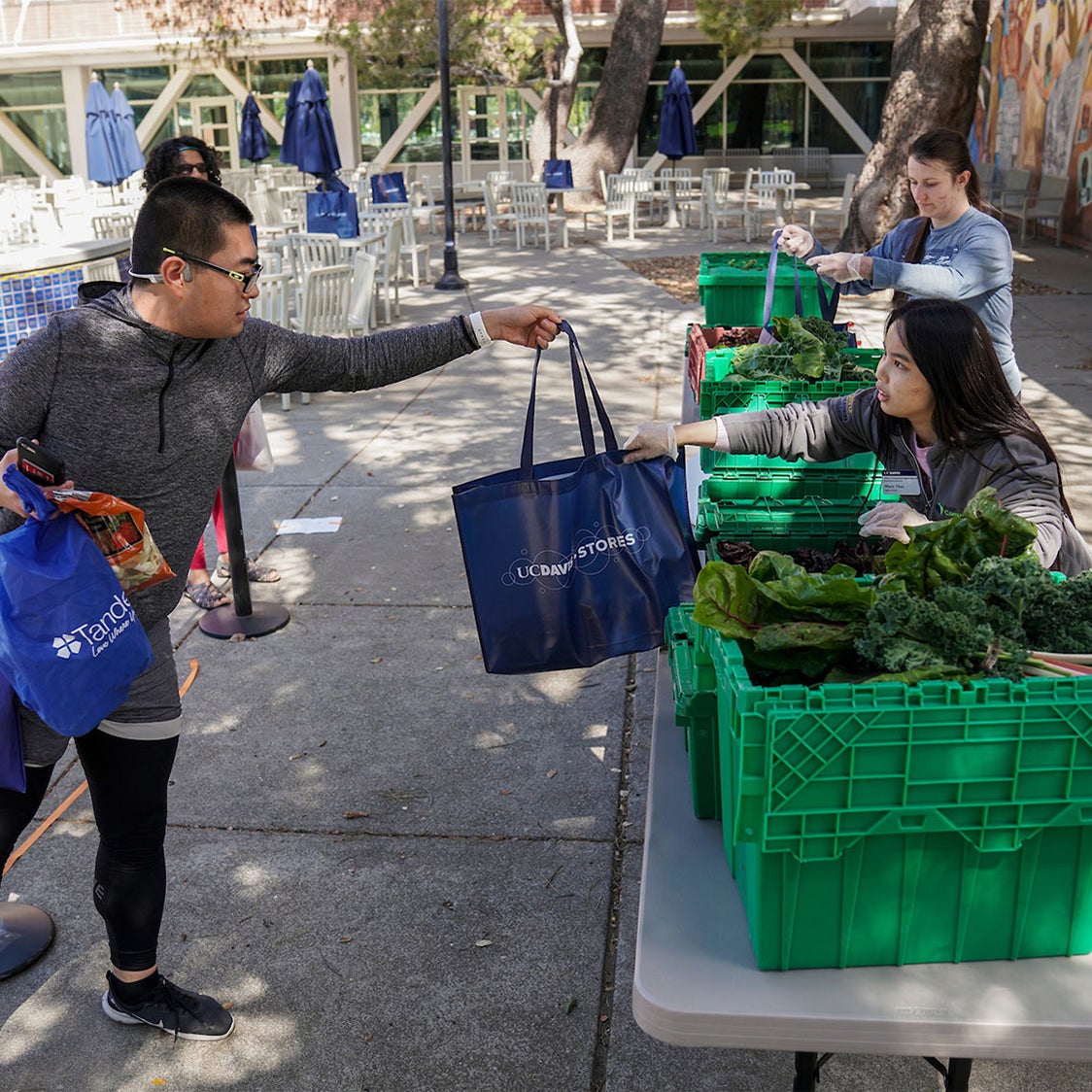 Student hands a bag of produce to another student outside the Memorial Union