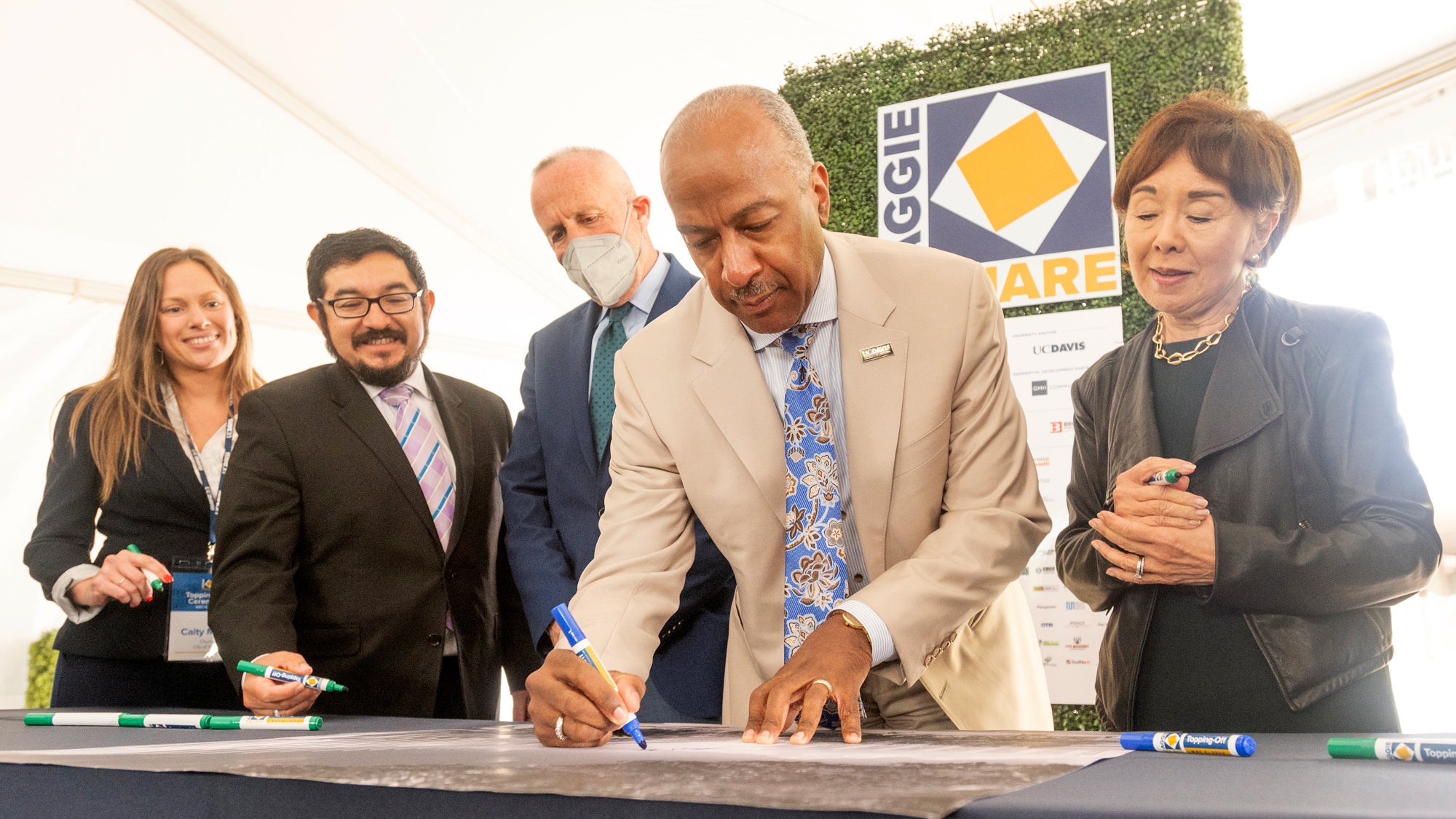 UC Davis Chancellor Gary S. May in tan suit signs Aggie Square poster