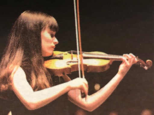 Teenager plays violin, in formal wear, on stage
