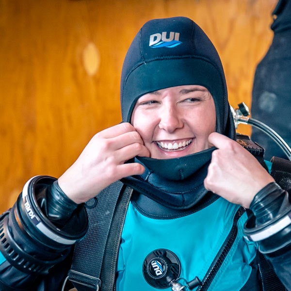 A diver smiles for the camera as she fits her wetsuit to her head.
