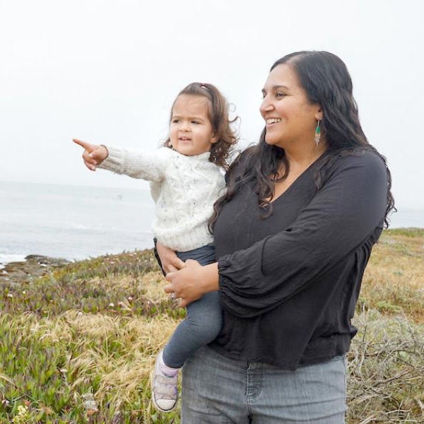 A person holds their baby on a bluff above the Pacific Ocean