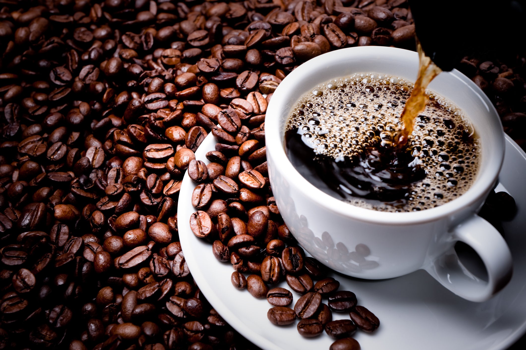 Coffee being poured into a cup surrounded by coffee beans