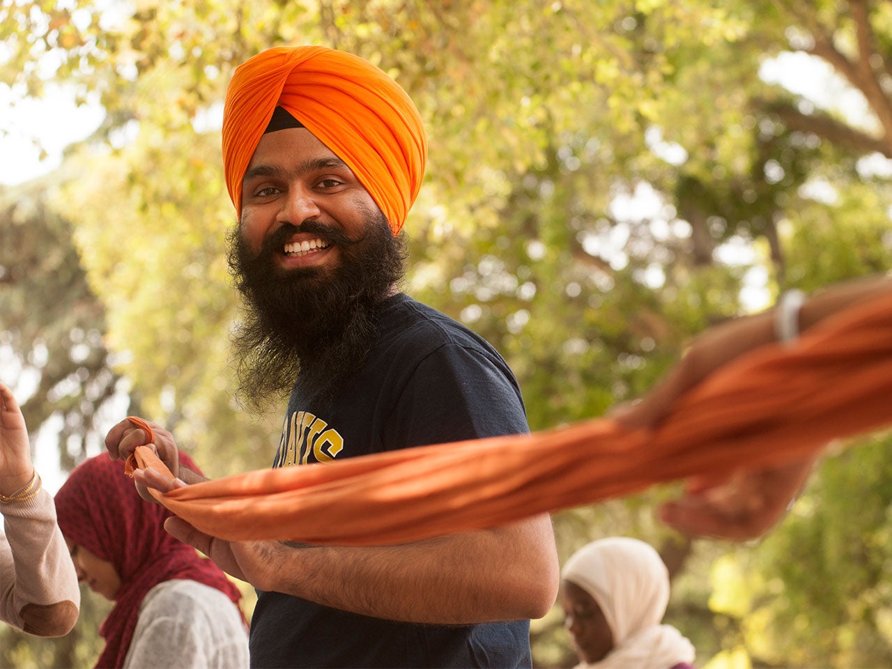 A UC Davis student smiles at the camera while stretching orange fabric.