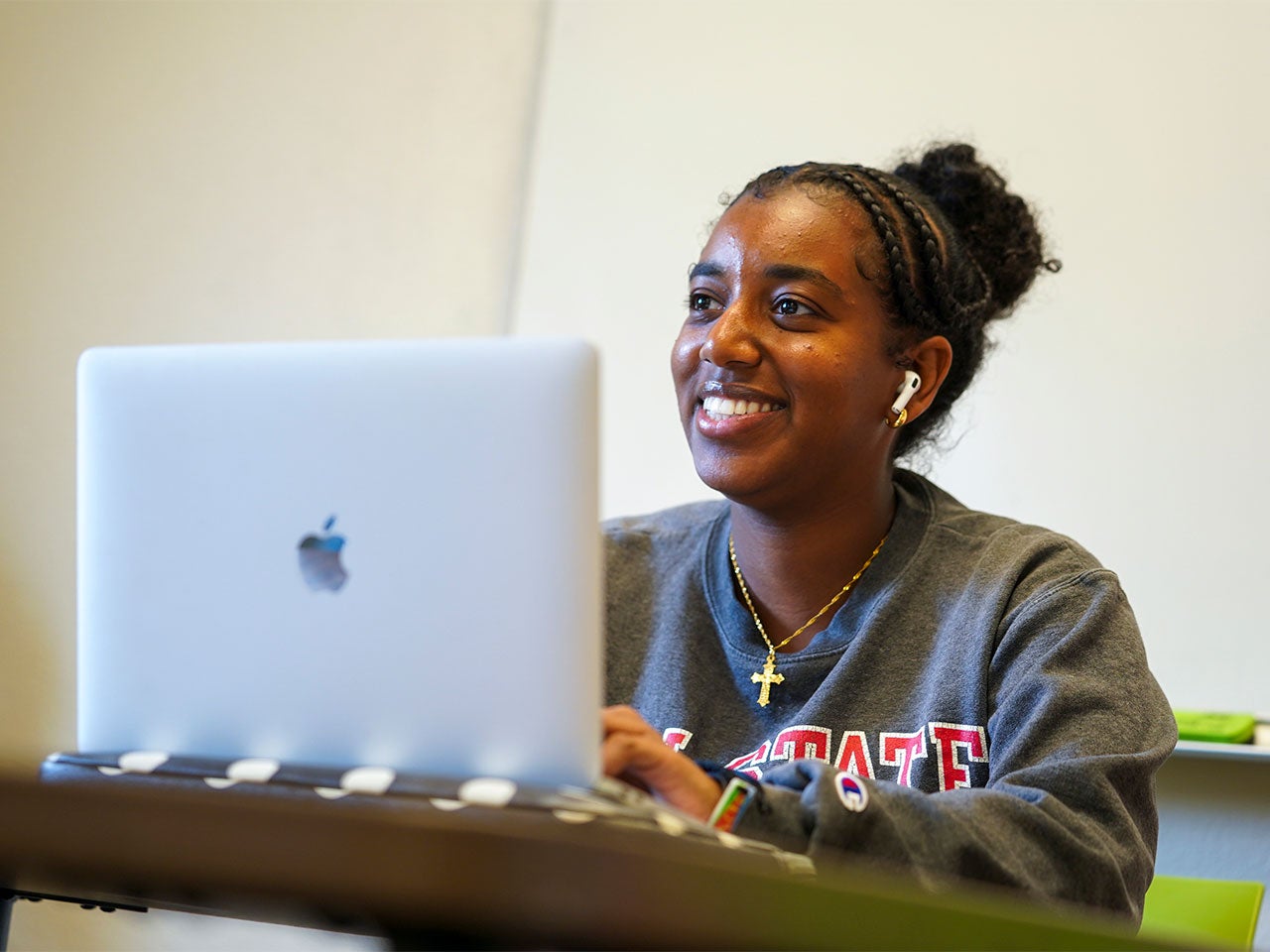 A UC Davis student smiles while typing on a silver laptop.