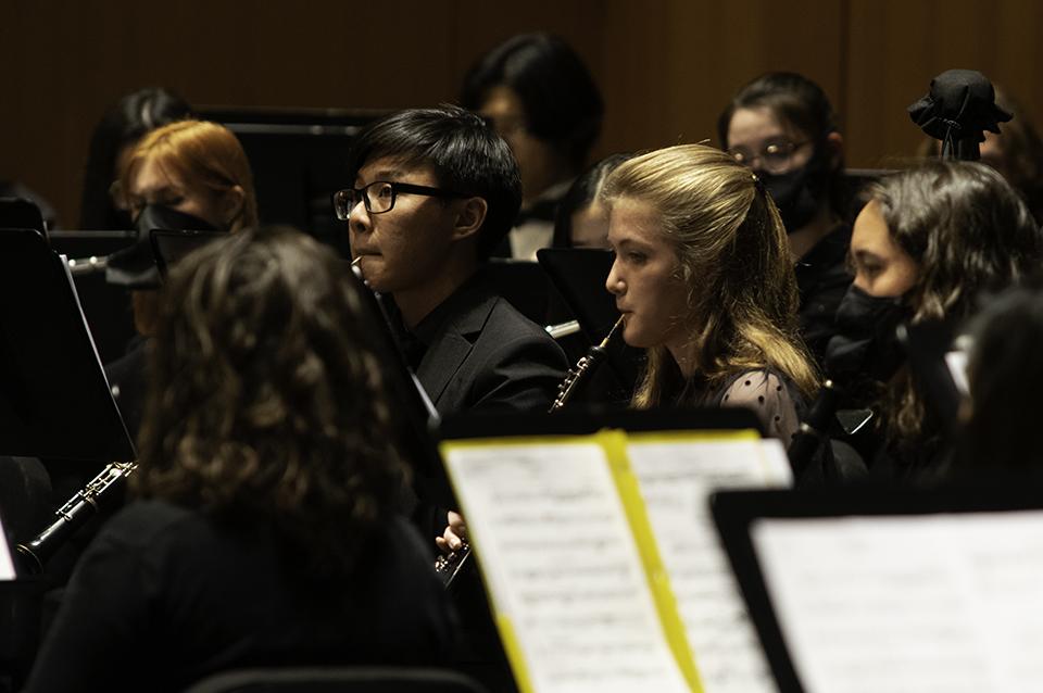 Members of concert band with instruments in performance, wearing black with dark background
