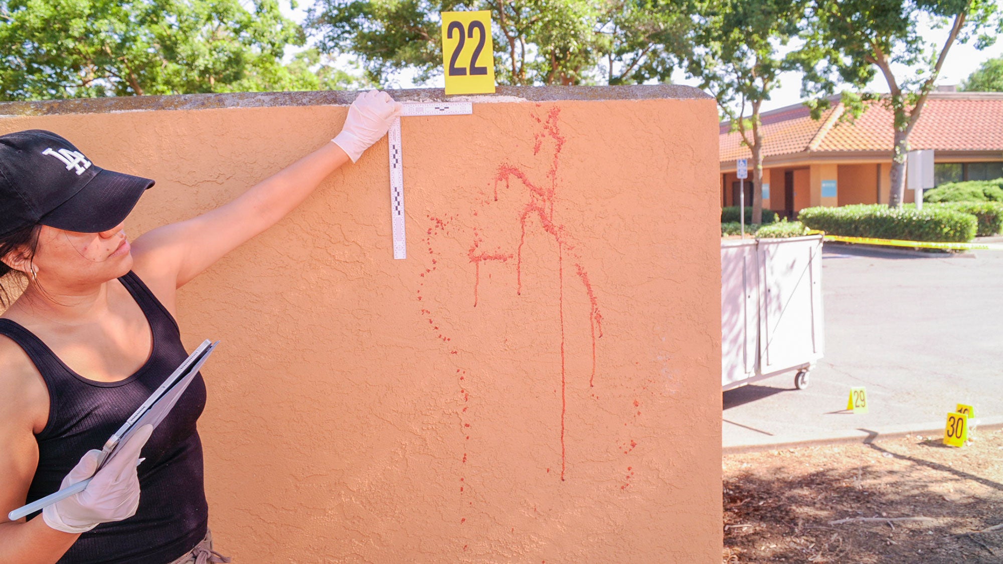 Woman analyzes red splatters on a wall with a yellow crime scene tag labeled 22