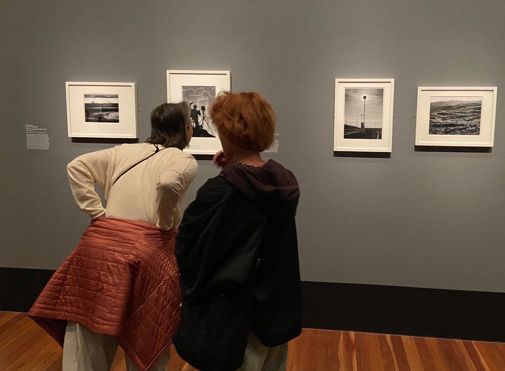 Art viewers look closely at black-and-white photographs in frames on gray wall in museum