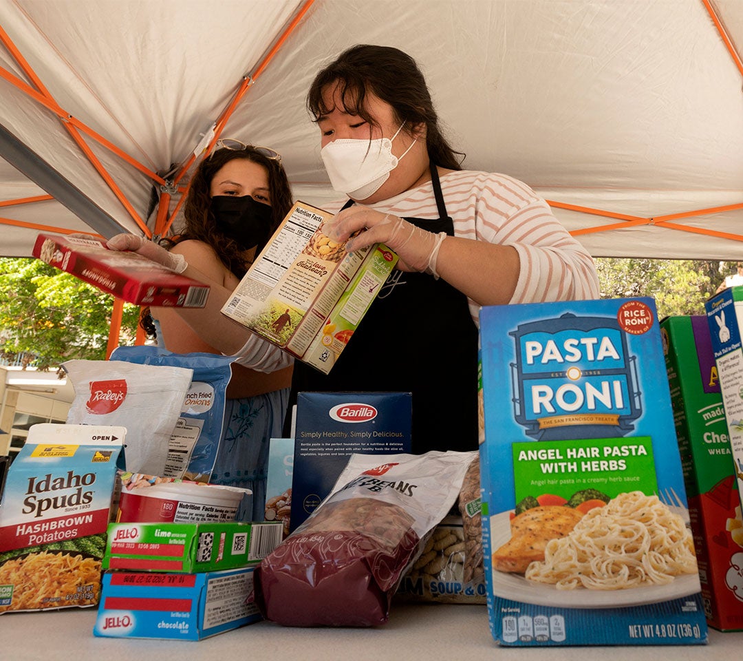 Students wearing face masks organize food items under a tent for the Eat Well Yolo program at UC Davis, aiding in community partnership and support.