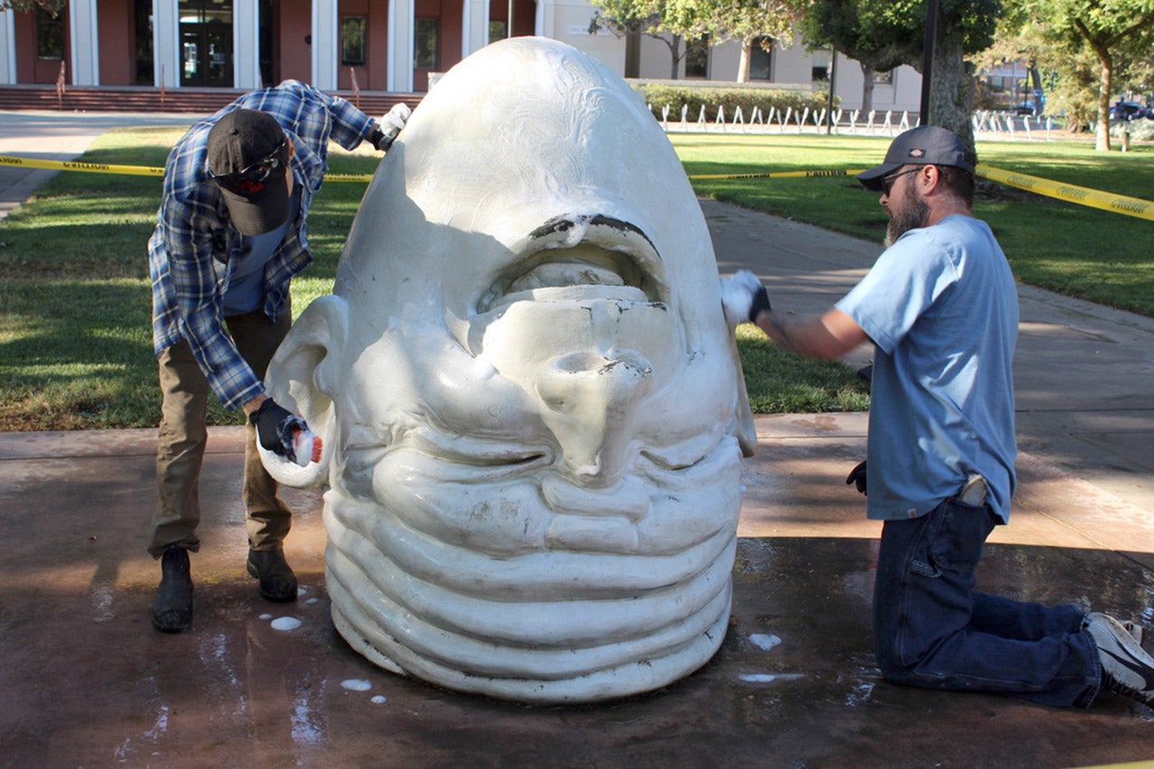 Two workers scrub an Egghead sculpture.