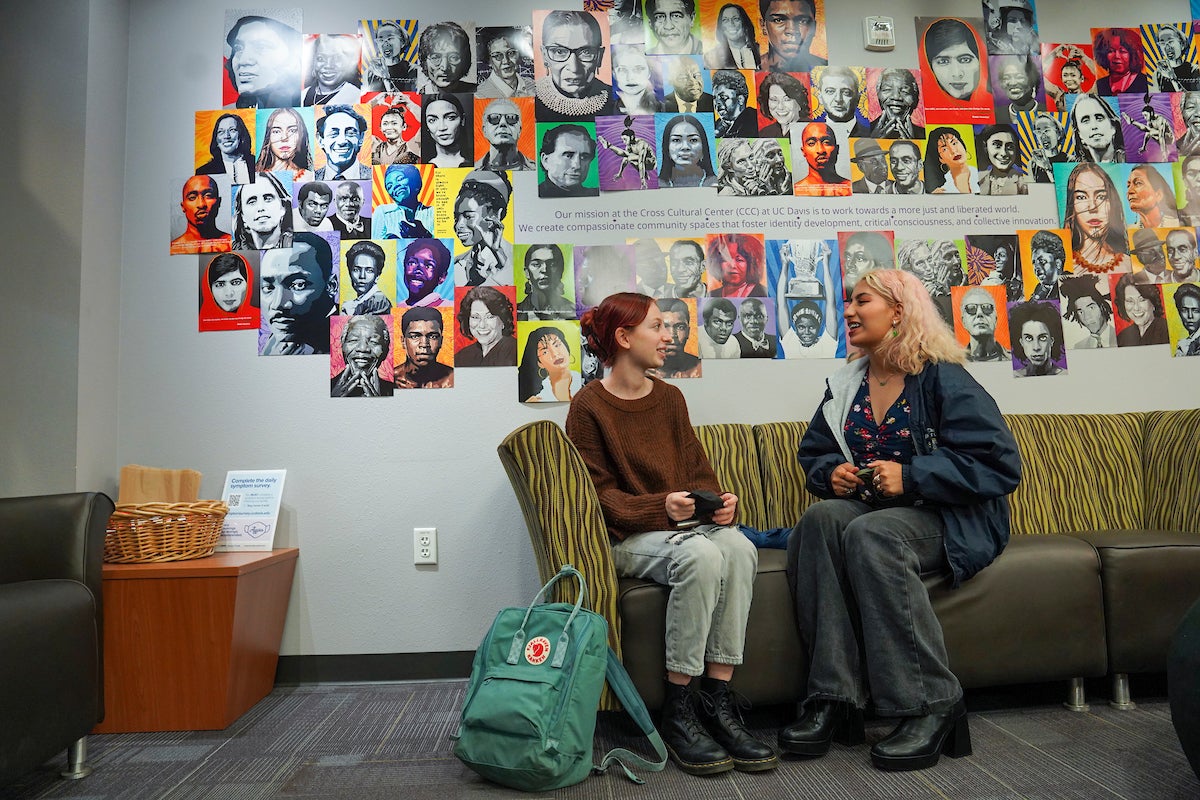 Two students chat on a couch in front of a bright mural at UC Davis. 