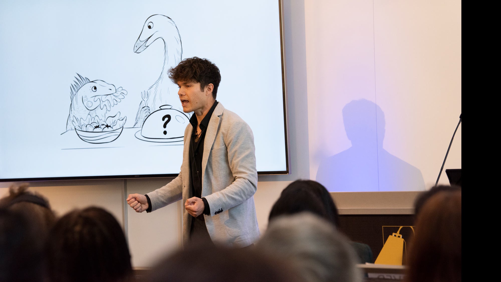 Man gestures during presentation, with drawing of reptiles behind him, on a slide