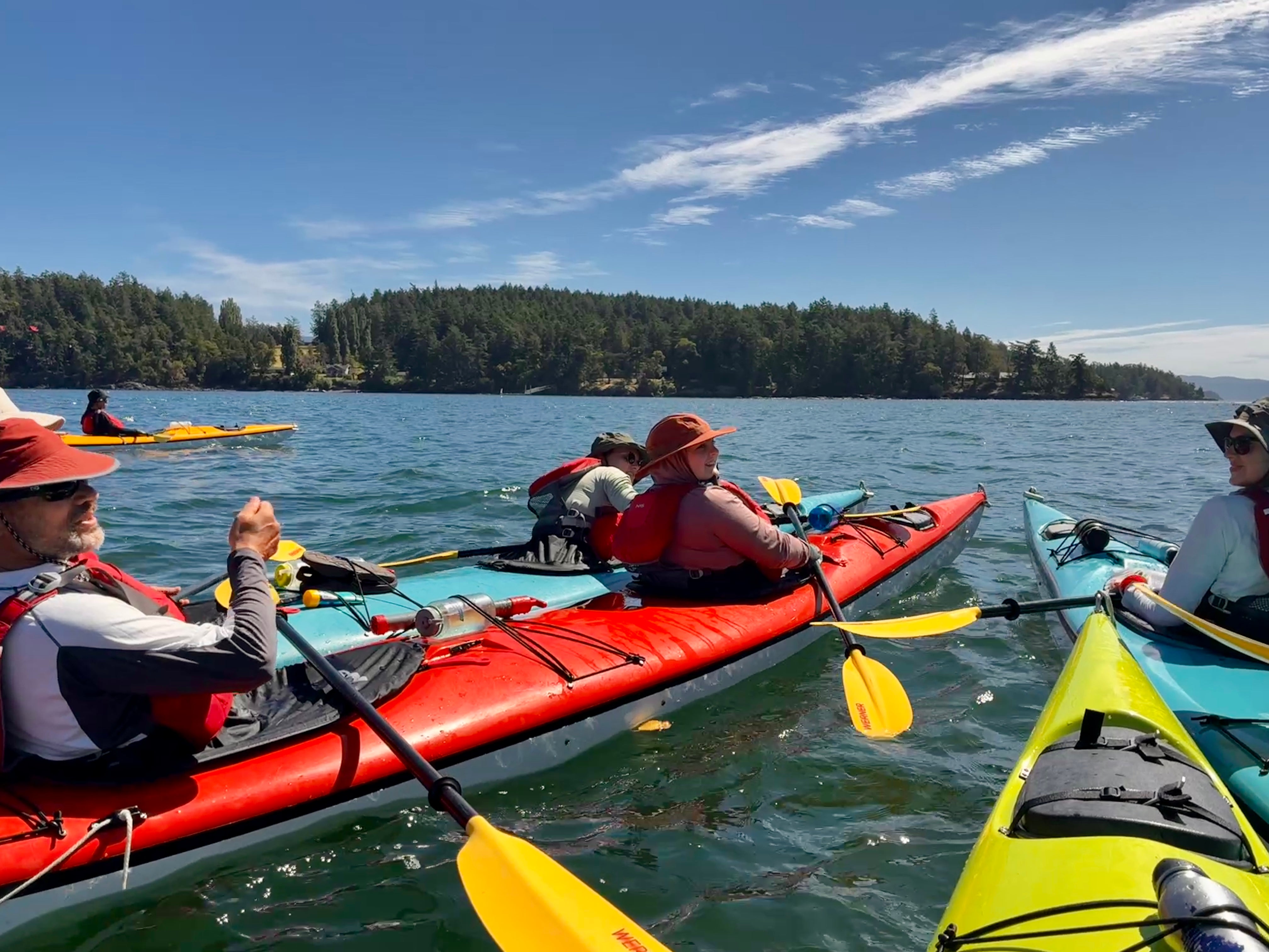 Group of kayakers in colorful kayaks on calm blue lake near forested shore