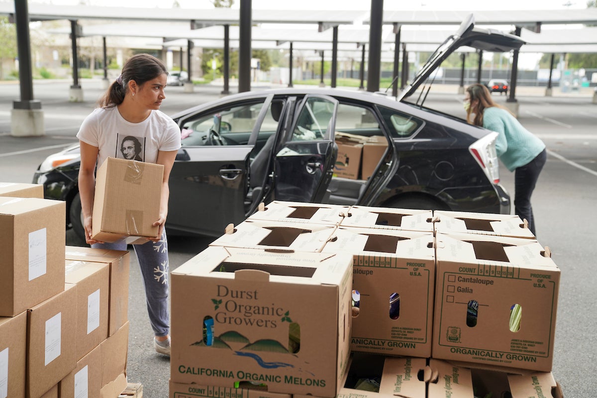 Volunteers load boxes into the back of a car in a parking lot.