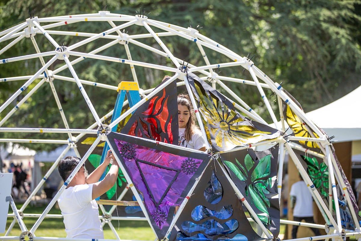 A volunteer and two children set up a colorful dome in a green field at UC Davis.
