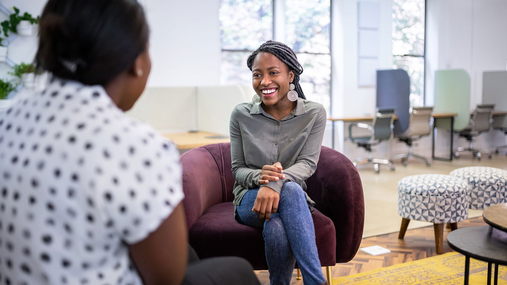 Smiling woman in grey talks with someone in bright office lounge.