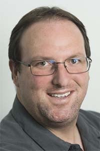 Smiling man with glasses in a casual headshot on a light gray background