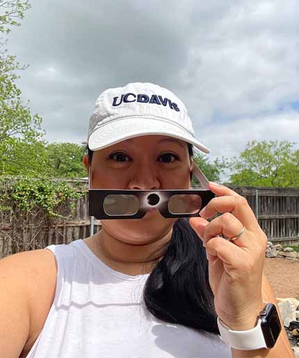 Karla Fung in UC Davis hat holds up eclipse glasses