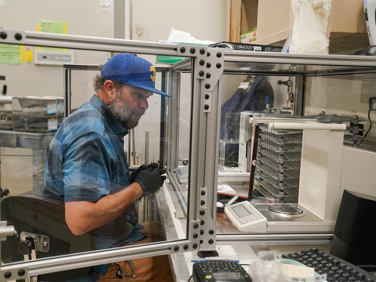 Keith Bein in a blue shirt and cap seated in lab at work on air quality research