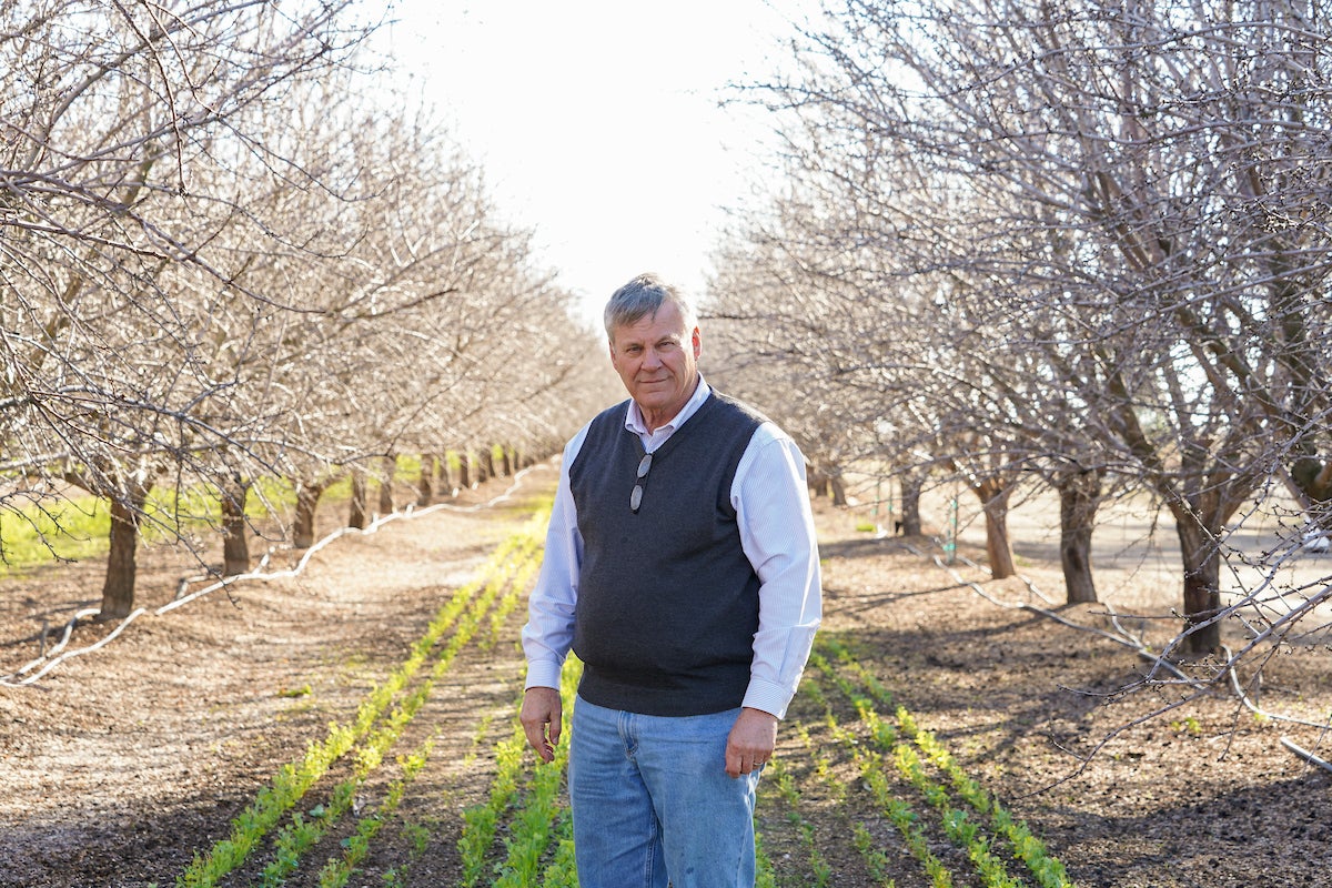 Kirk Pumphrey of Westwind Farms stands in front of his rows of almond trees in Yolo County, CA. He's using a precision metering and almond mulch to conserve groundwater. (Karin Higgins/UC Davis)