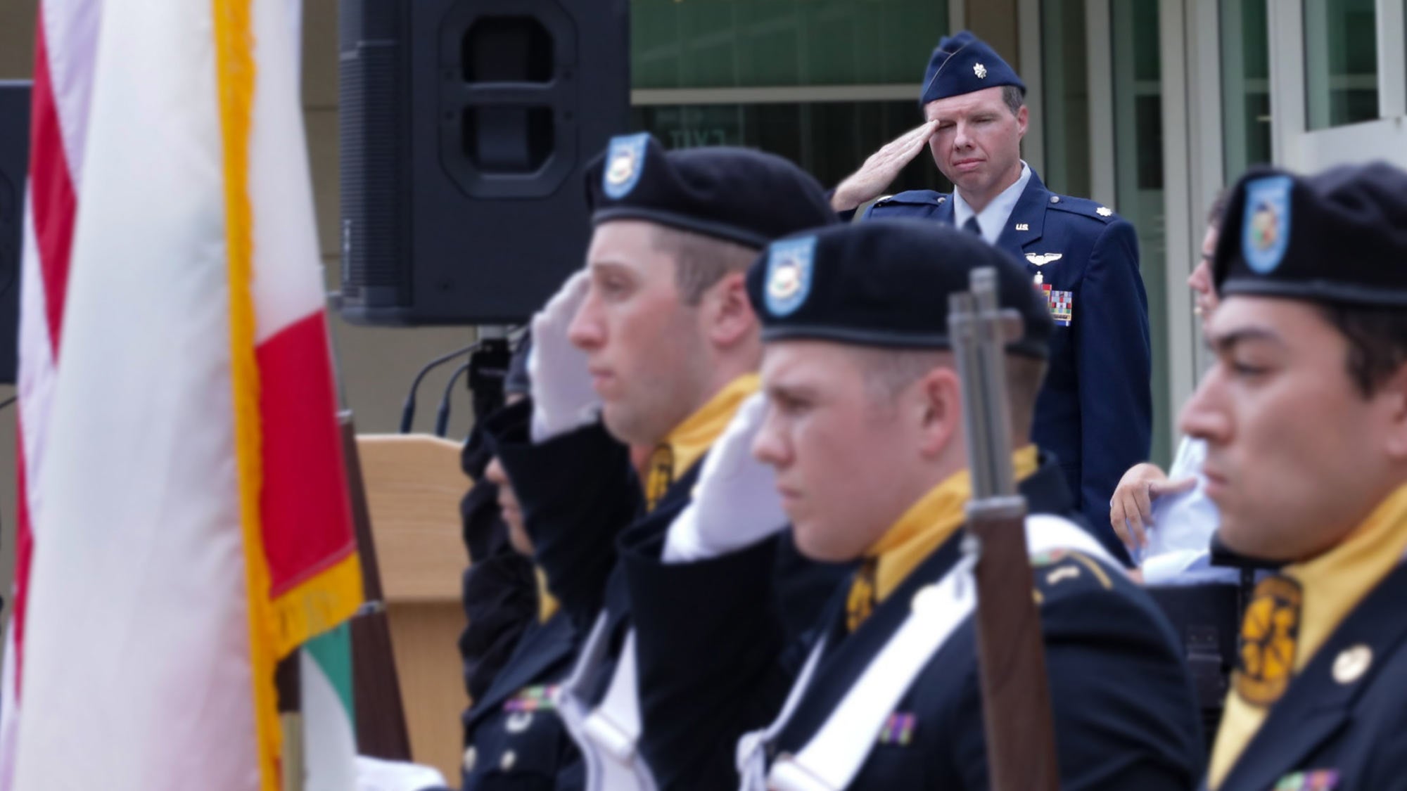 Air Force officer salutes, in background, behind color guard