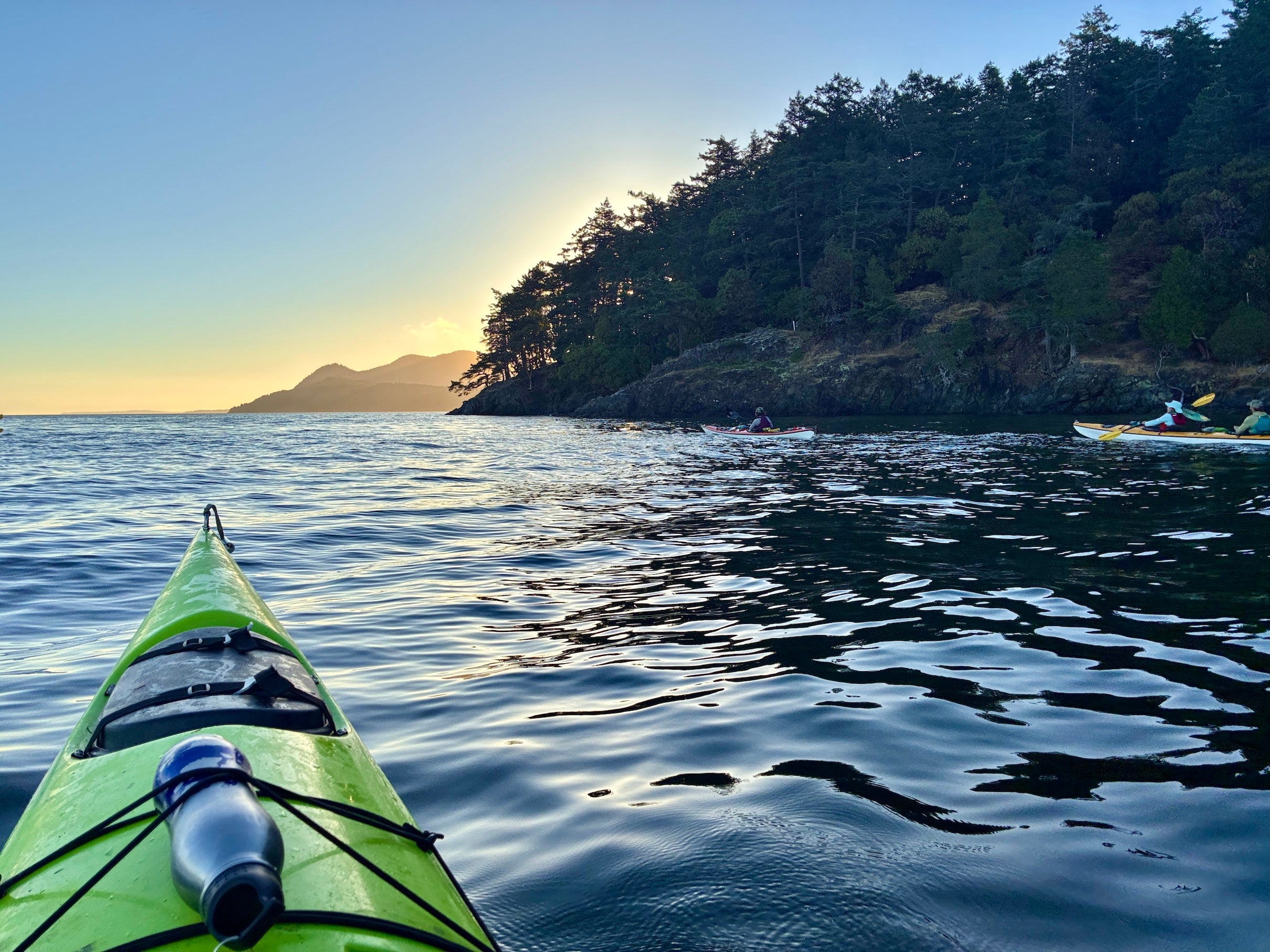 Serene green kayak bow on calm coastal water at sunrise with tree-covered headland