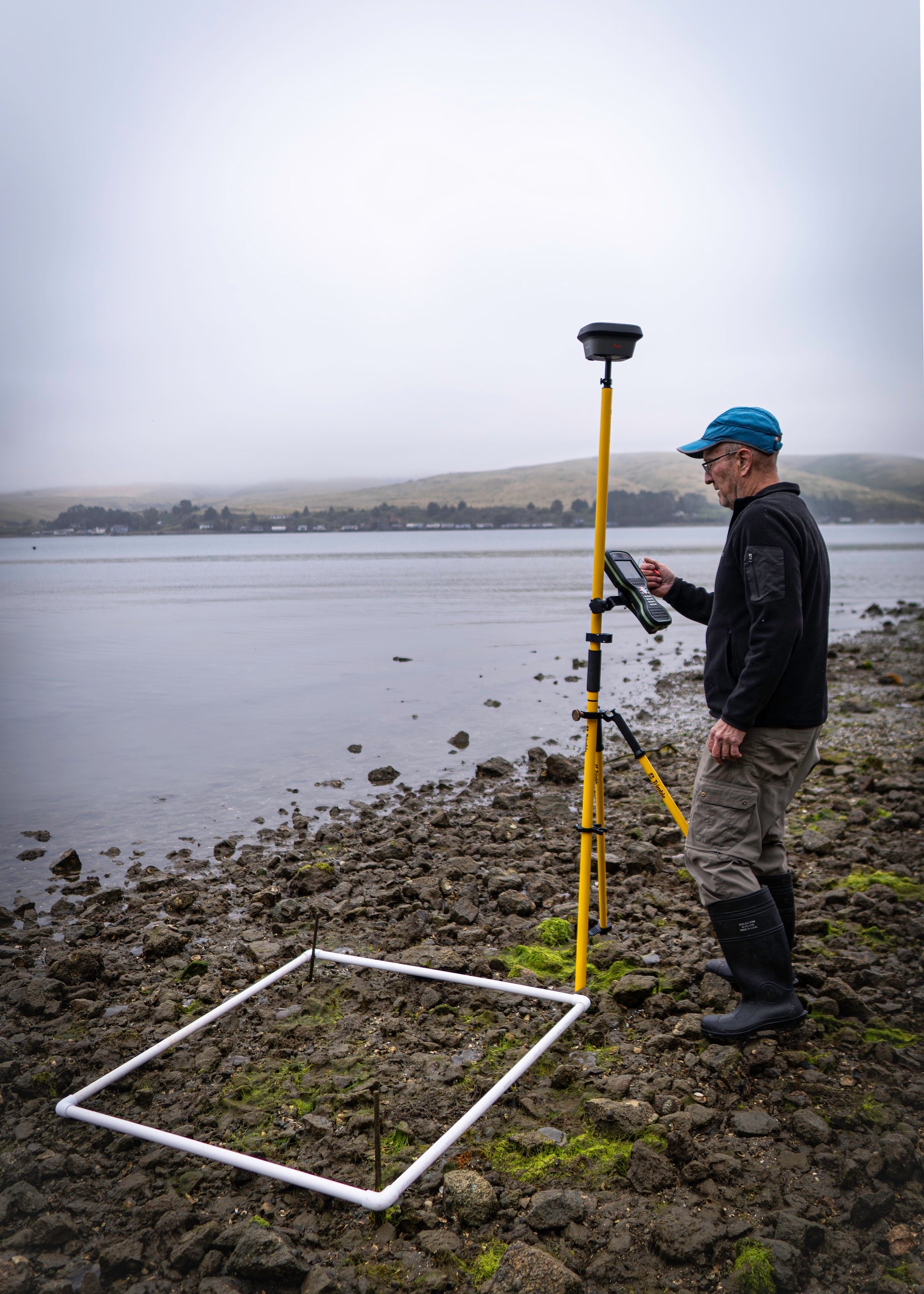 scientist Ted Grosholz in field clothing working with monitoring equipment along the edge of a rocky shore.