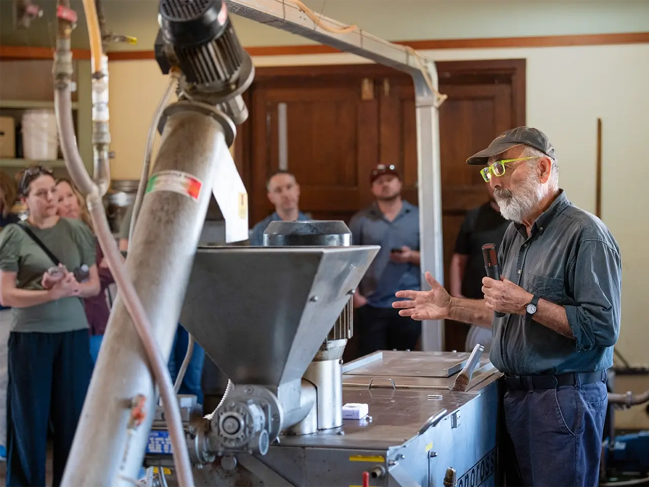 Group watching worker operate industrial machinery in sunlit wood‑beamed workshop