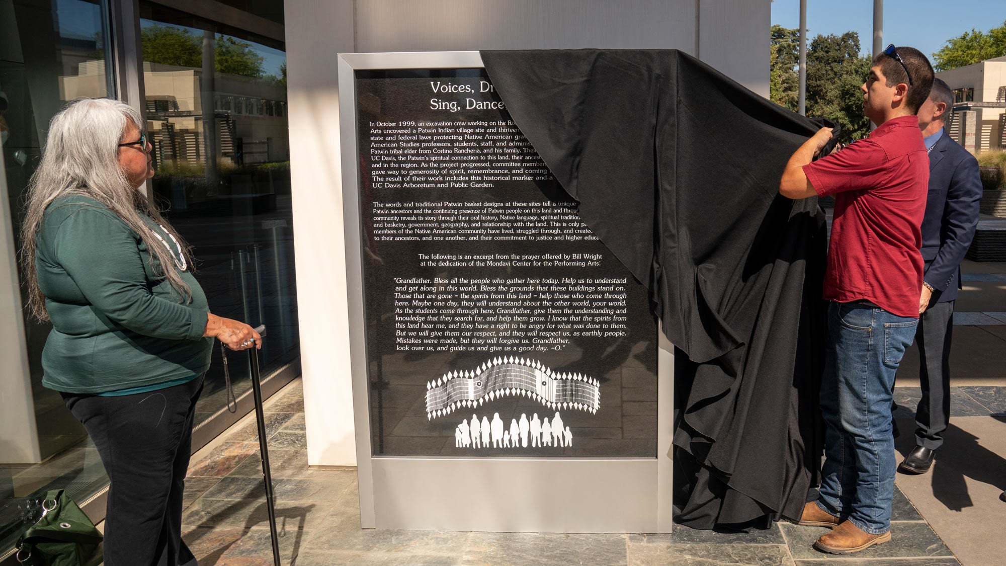 Woman looks on as man lifts cover off of monument.