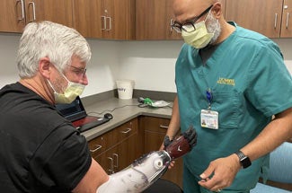 Medical professional in scrubs examines man's prosthetic hand