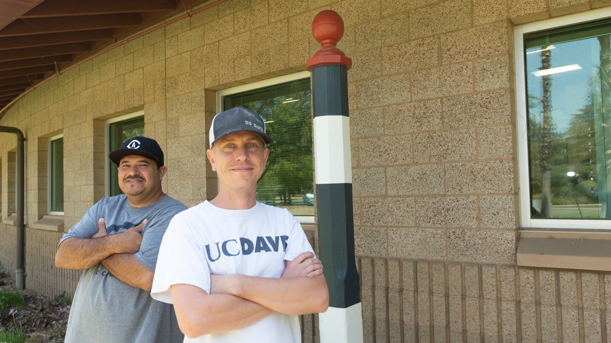 Two men from campus Paint Shop, posing in front of racetrack distance pole.