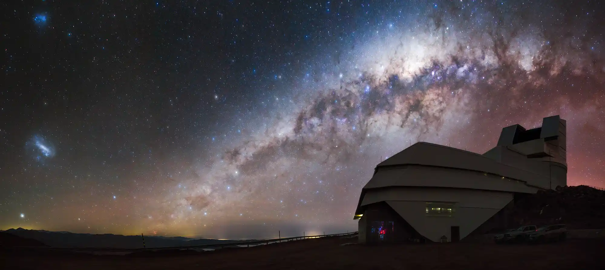 Modern observatory silhouette under vibrant Milky Way arching across starry sky