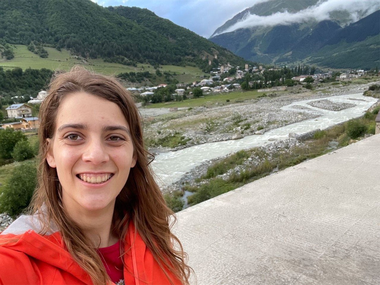 UC Davis Russian major Darian Lee poses smiling in front of a mountain vista near Tbilisi, Georgia. In the valley below, a town is visible.