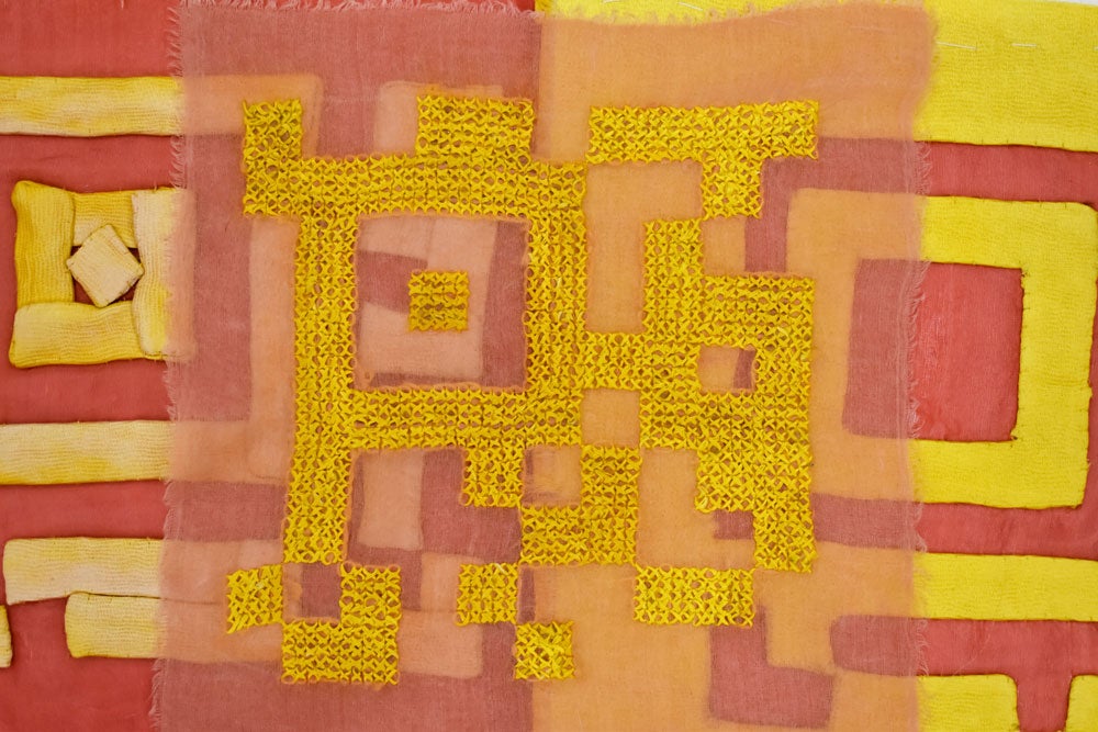 Bright orange X stitches create a square pattern on transparent red fabric. Behind the stitching are painted red and yellow square shapes.