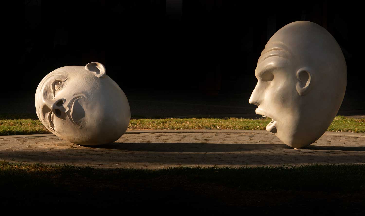Two Egghead sculptures looking at each other in lighted darkness