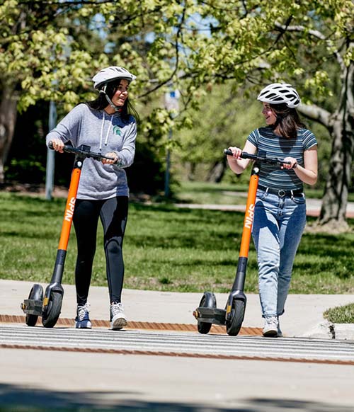 Two people walk with Spin scooters
