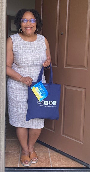 Woman stands in open doorway of home, holding gift bag.