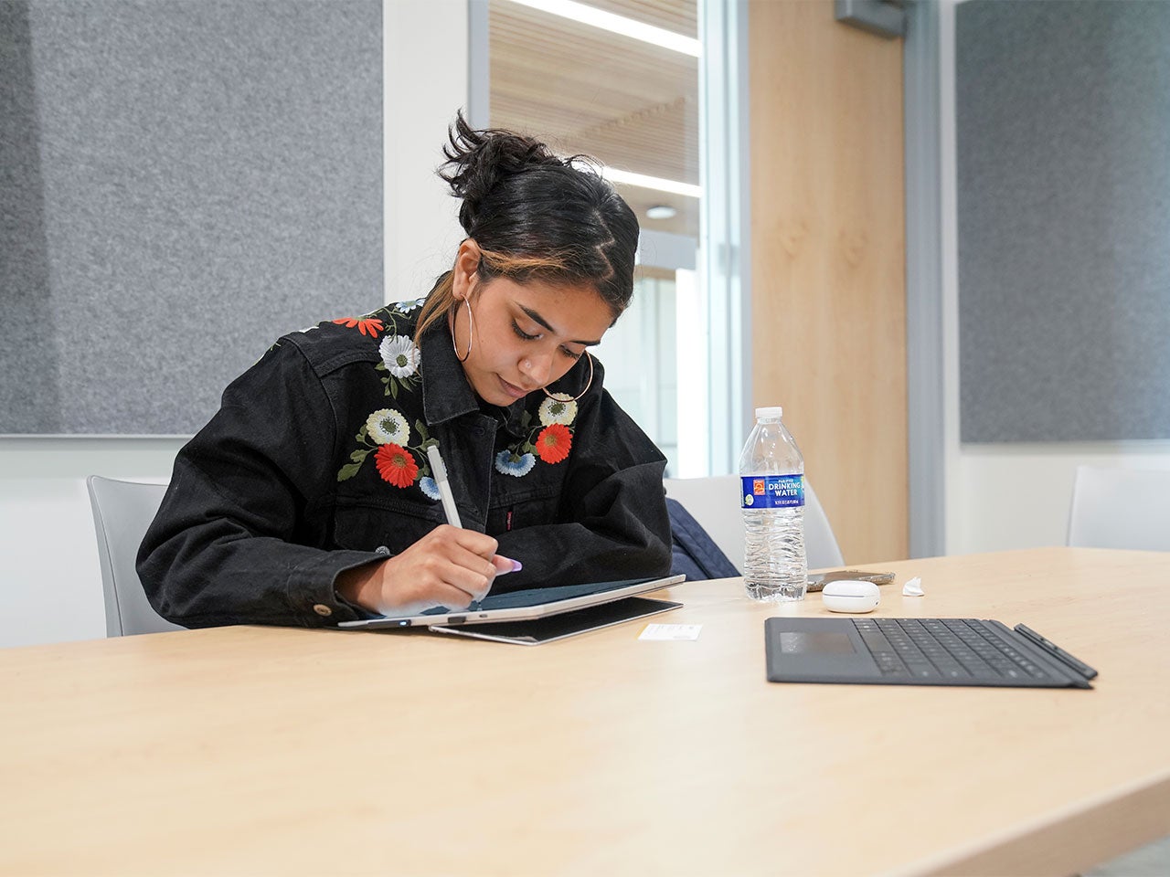A UC Davis student, wearing hoop earrings and a black denim jacket with floral embroidery, takes notes on a tablet in UC Davis' Center for Educational Effectiveness.