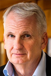 Close-up portrait of man with gray hair, neutral expression, warm indoor background
