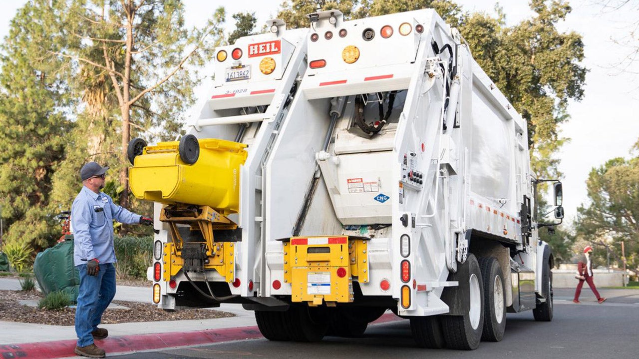 A worker empties a trash can into a truck.
