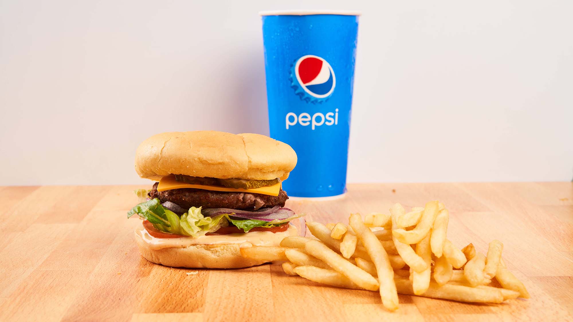 Buger, fries and Pepsi cup photographed on wood table