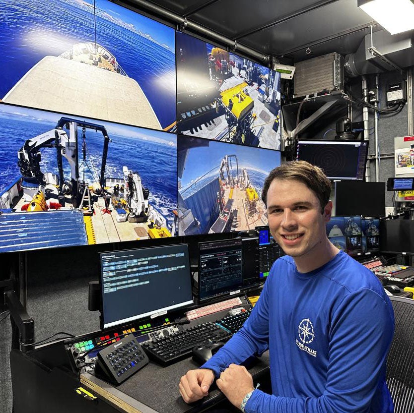 Smiling man at marine control console with multiple large underwater video screens