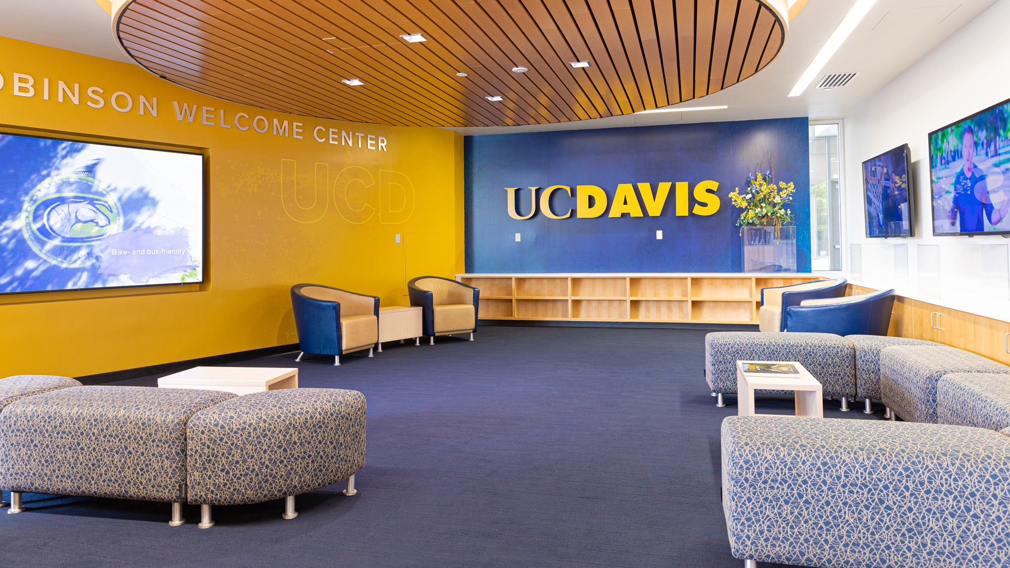 Lounge furniture in room with "UC Davis" on one wall, digital screens on two others