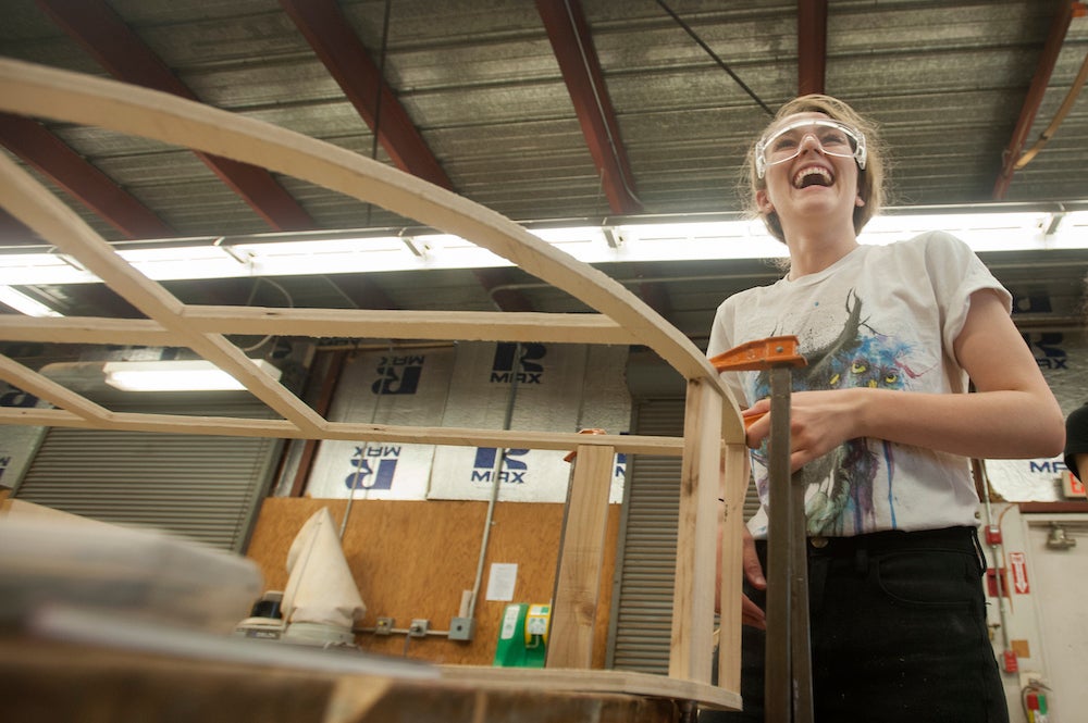 A student wearing goggles laughs beside the scaffolding of her furniture at UC Davis. 