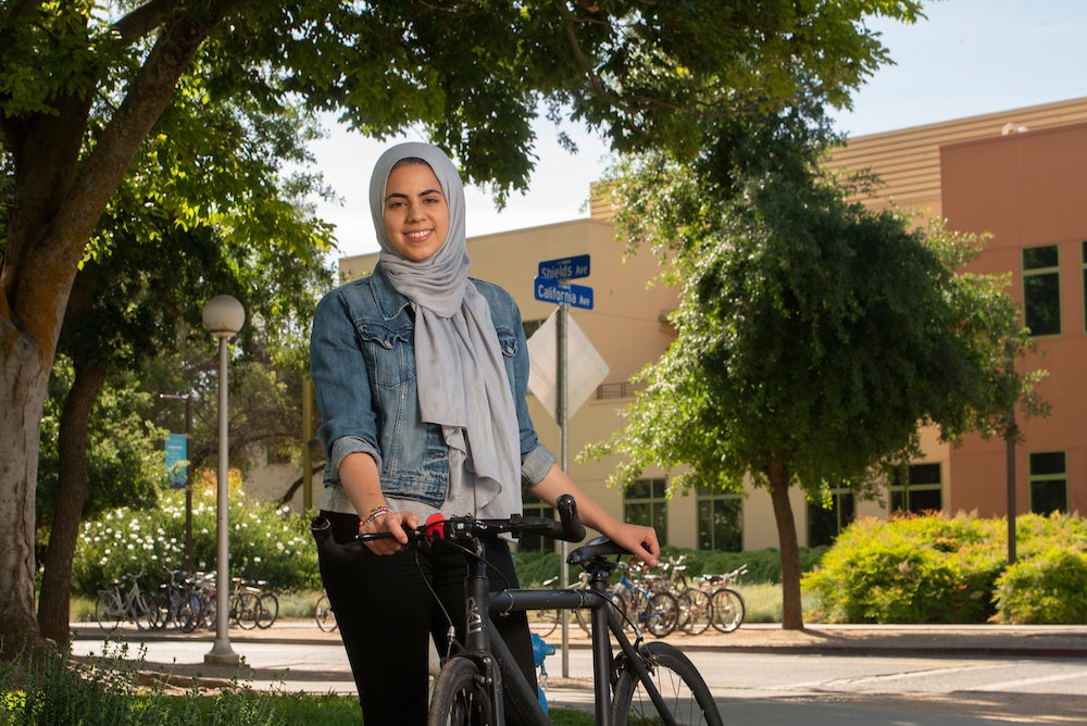 A political science major stands on the UC Davis campus with her bike.