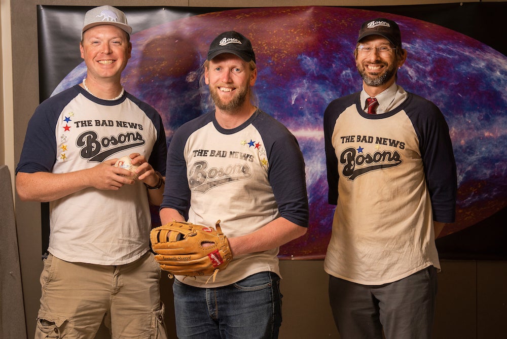 Three men in baseball jerseys pose in front of a galaxy screen at UC Davis. 
