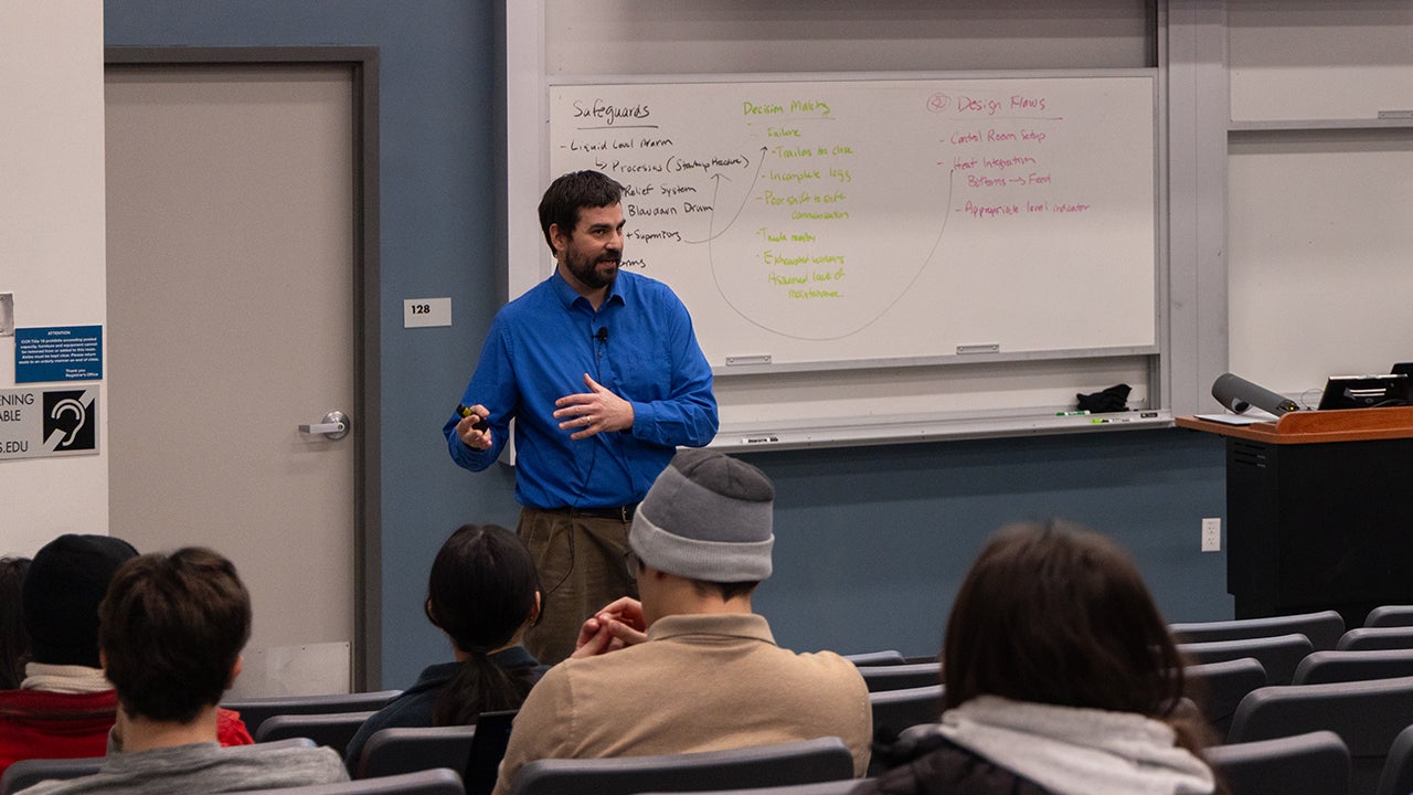 Instructor in blue sweater speaking to seated students in classroom